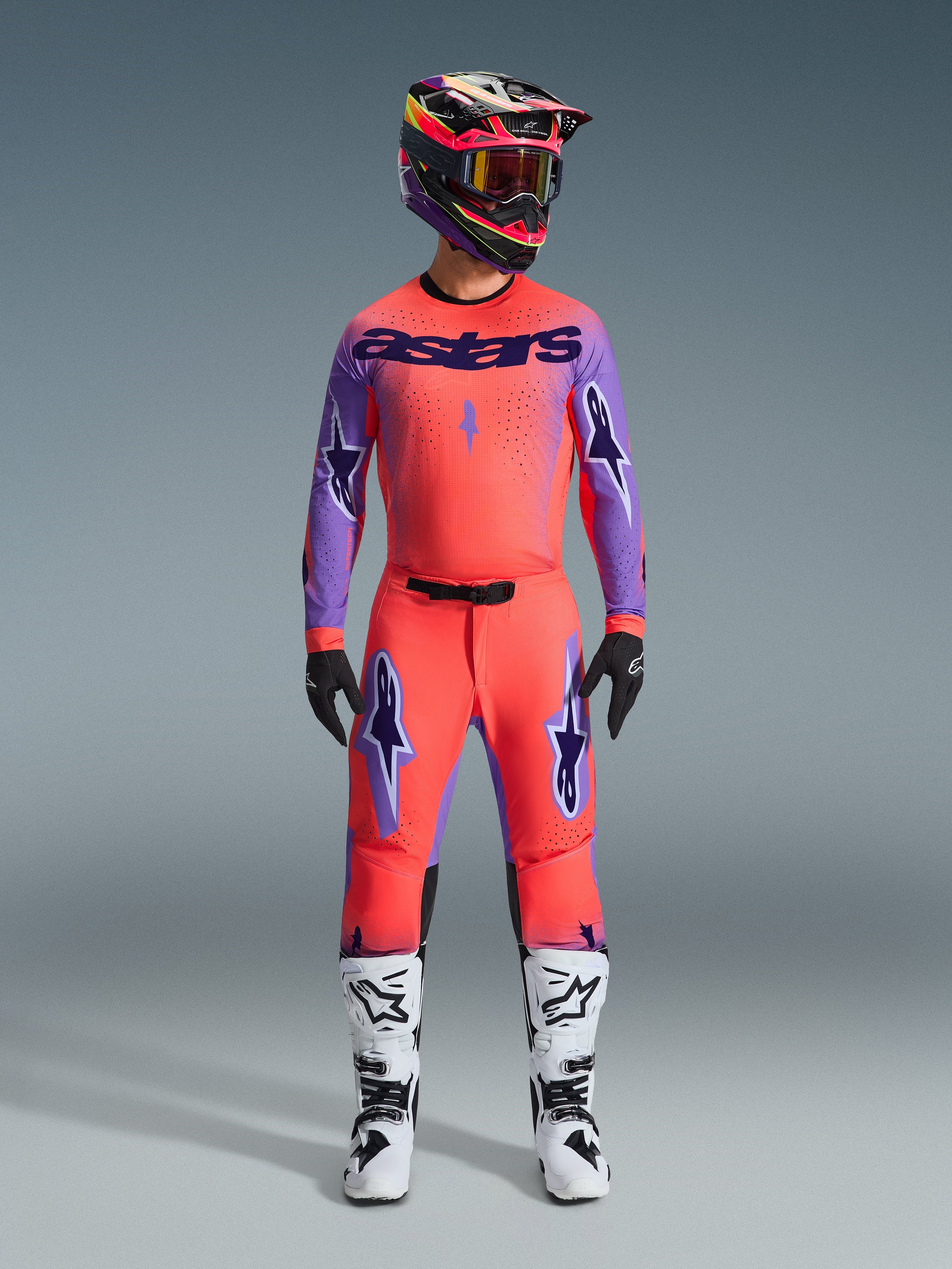 Conjunto Supertech Scenz 2026, equipación de motocross Alpinestars, rojo anaranjado vibrante y púrpura, jersey con la marca 'astars' en negro, pantalones a juego con logotipos de estrellas púrpura, casco de competición colorido y botas blancas, kit de rendimiento profesional para off-road
