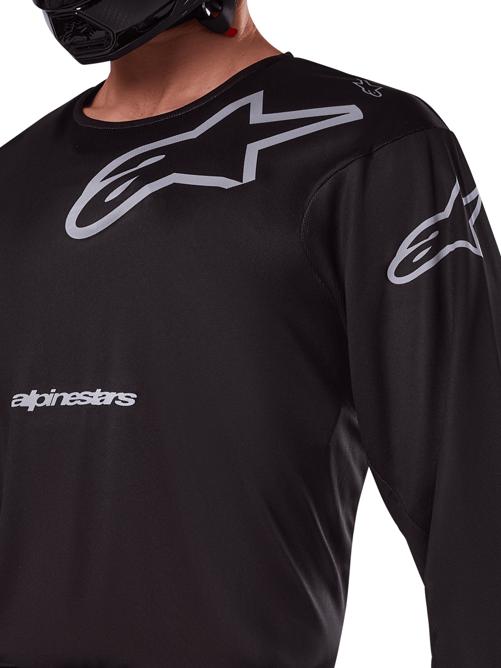 Alpinestars 2025 Racer Graphite Jersey, negro y gris, primer plano de piloto con jersey de motocross, con marca Alpinestars y logotipos A-star en gris, material de politejido técnico para conducción fuera de carretera