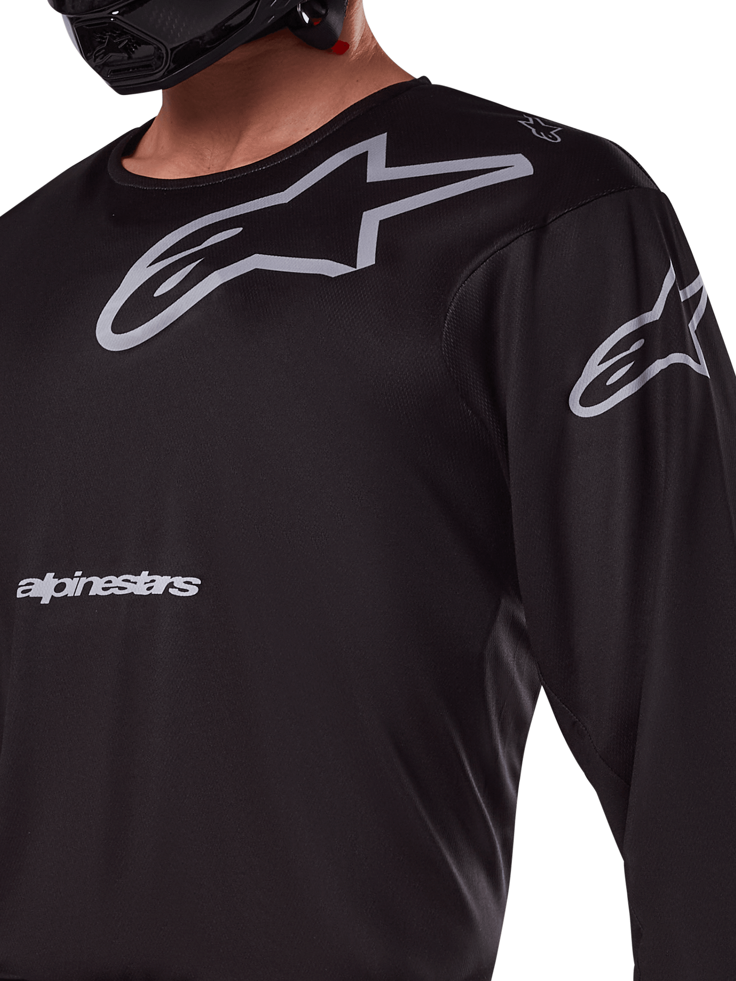 Alpinestars 2025 Racer Graphite Jersey, negro y gris, primer plano de piloto con jersey de motocross, con marca Alpinestars y logotipos A-star en gris, material de politejido técnico para conducción fuera de carretera