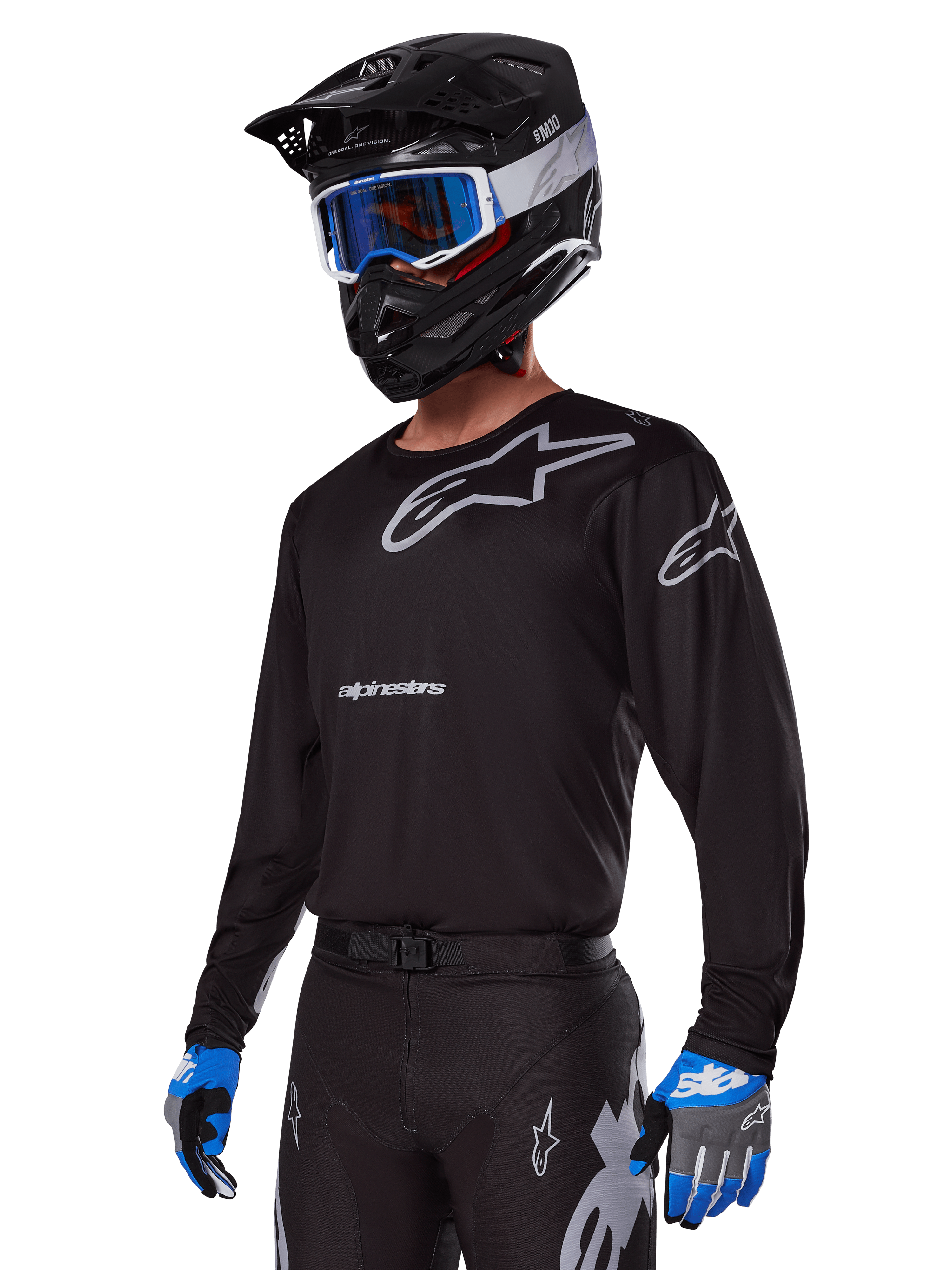 Piloto de motocross con el conjunto de equipo Alpinestars 2025 Racer Graphite, jersey negro con logotipos Alpinestars en gris, pantalones negros a juego con detalles grises, casco negro con gafas azules y blancas, guantes azules y grises, atuendo técnico estilizado para carreras fuera de carretera