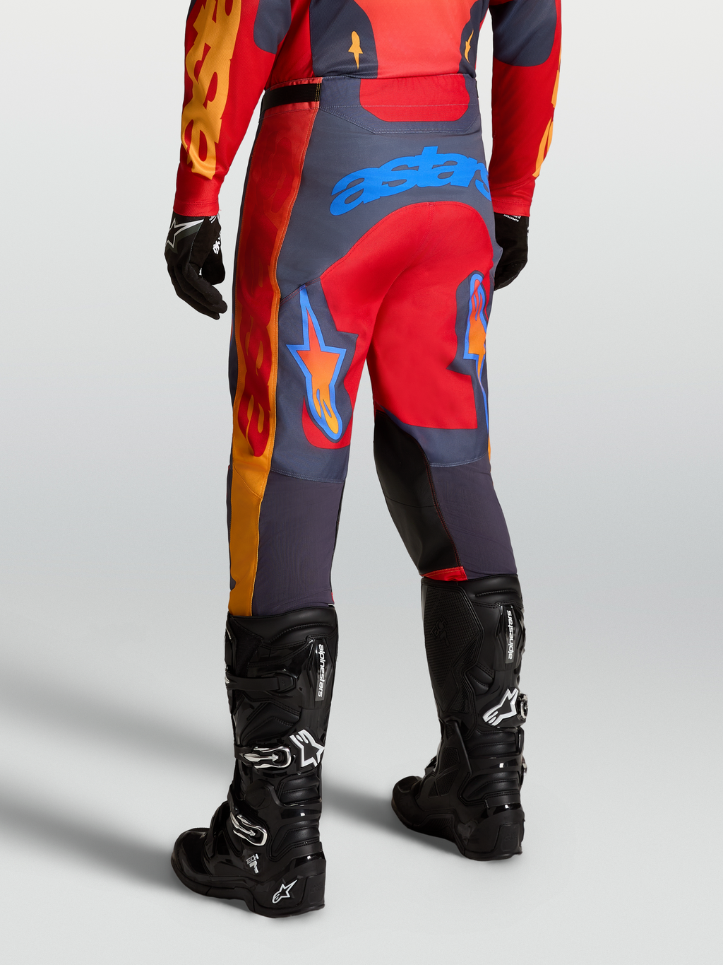 Alpinestars Pantalones Racer Hunt, pantalones técnicos de motocross, rojos y grises, mostrados desde atrás en posición de conducción deportiva