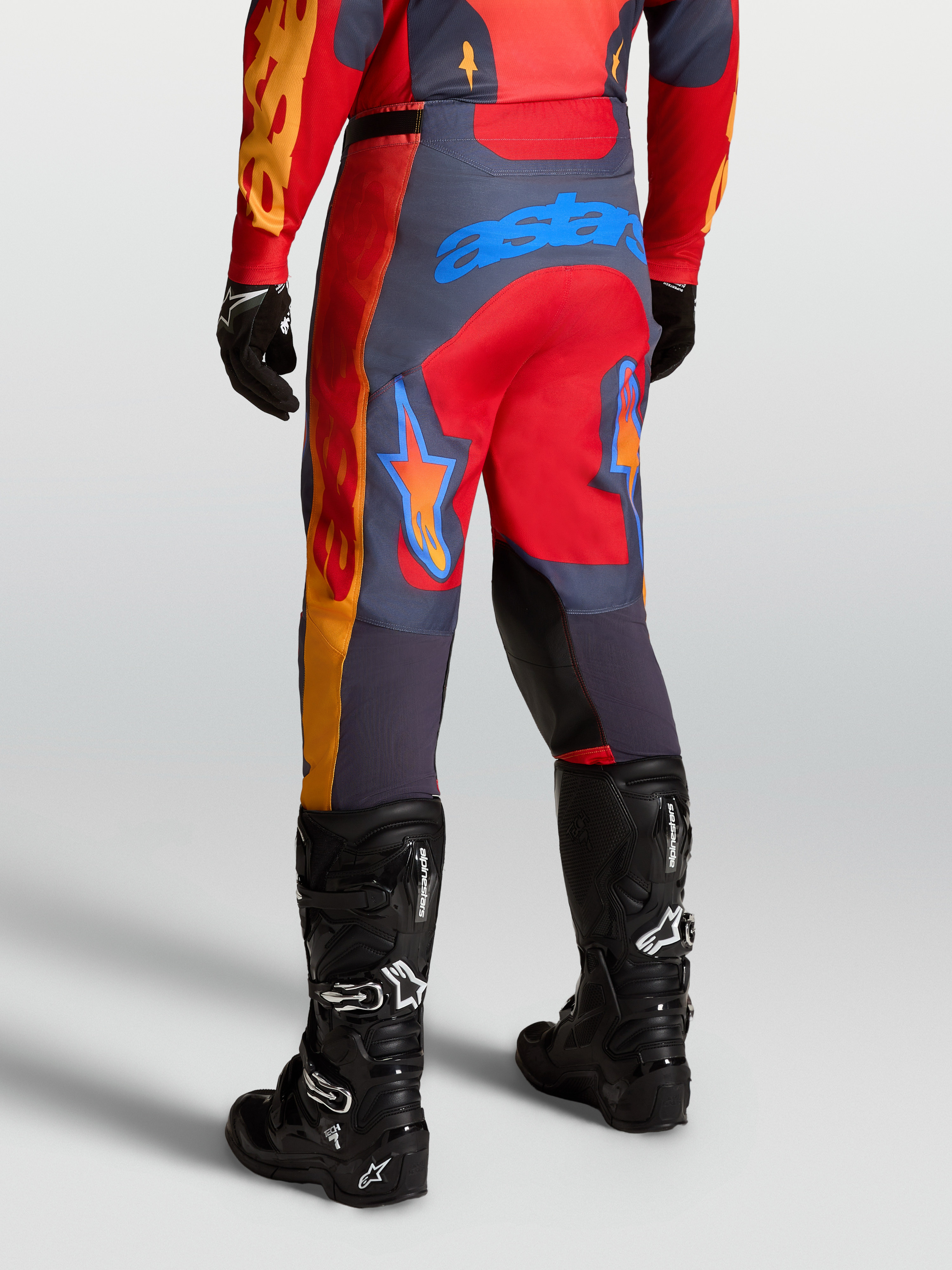 Alpinestars Pantalones Racer Hunt, pantalones técnicos de motocross, rojos y grises, mostrados desde atrás en posición de conducción deportiva