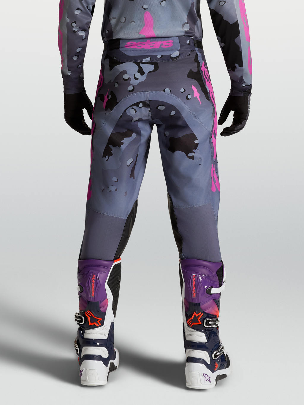 Alpinestars Racer Lone, pantalones de motocross para hombre, camuflaje gris y morado, vista trasera sobre modelo con botas MX a juego