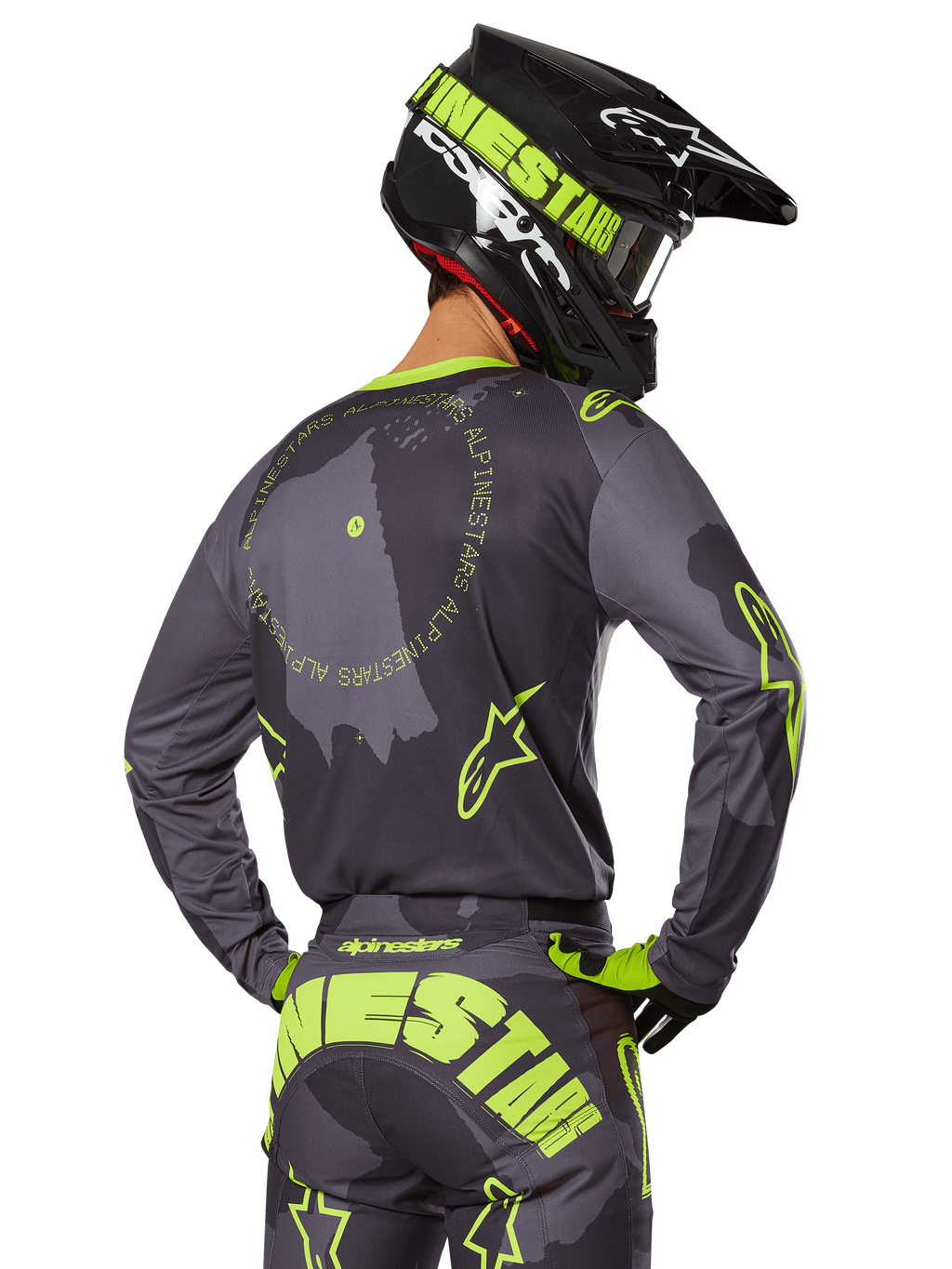 Piloto de motocross visto desde atrás con el conjunto de equipamiento Racer Hollow 2025, jersey gris con texto circular y logotipos de estrellas en amarillo fluorescente, pantalones grises y amarillos a juego con marca llamativa en el asiento, casco negro y verde lima, atuendo coordinado para carreras fuera de carretera