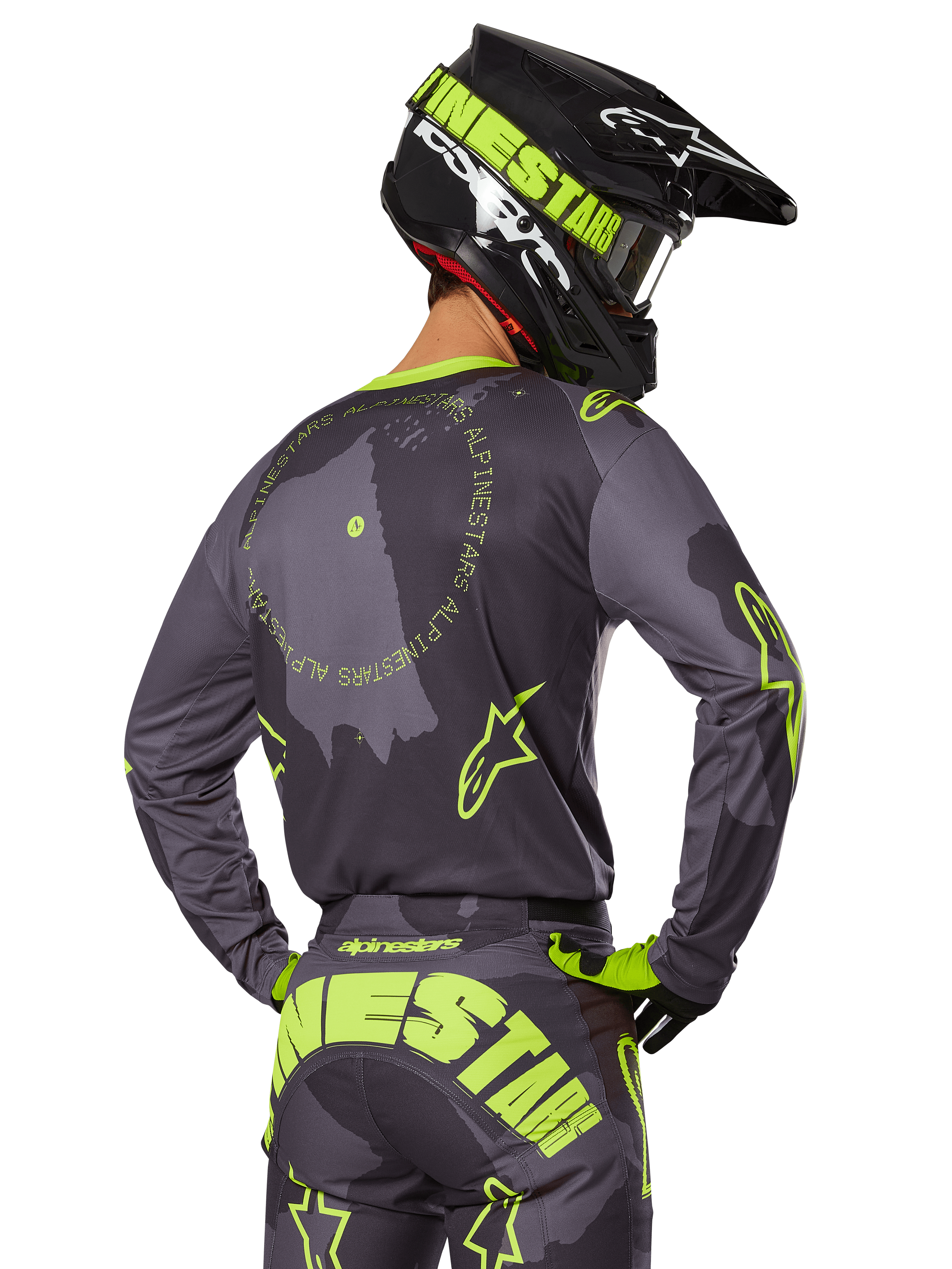 Piloto de motocross visto desde atrás con el conjunto de equipamiento Racer Hollow 2025, jersey gris con texto circular y logotipos de estrellas en amarillo fluorescente, pantalones grises y amarillos a juego con marca llamativa en el asiento, casco negro y verde lima, atuendo coordinado para carreras fuera de carretera
