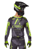 Alpinestars 2025 Racer Hollow Jersey, jersey de motocross, camuflaje oscuro y amarillo neón, combinado con pantalones a juego, casco negro y amarillo con gafas, y guantes negros, con la marca Alpinestars y diseño de camuflaje