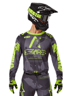 Alpinestars 2025 Racer Hollow Jersey, jersey de motocross, camuflaje oscuro y amarillo neón, combinado con pantalones a juego, casco negro y amarillo con gafas, y guantes negros, con la marca Alpinestars y diseño de camuflaje