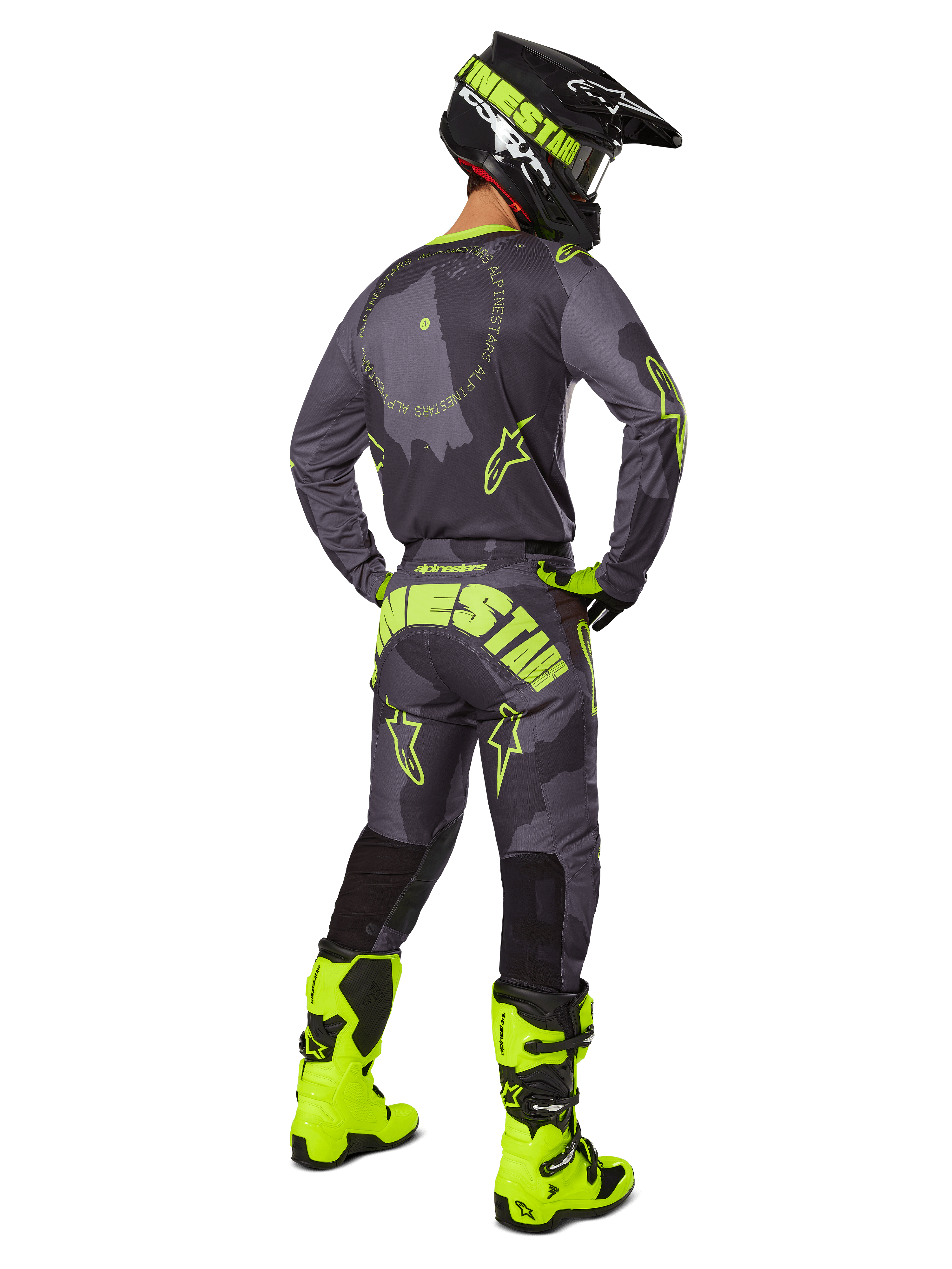 Vista posterior de un piloto de motocross que viste el conjunto Racer Hollow 2025 en color Dark Camo Yellow Fluo, con un jersey de camuflaje gris con detalles en amarillo flúor, pantalones de motocross a juego con un logotipo llamativo en el asiento, botas amarillo flúor vibrante y un casco negro con gafas amarillas.