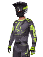 Conjunto de equipo Alpinestars Racer Hollow 2025, jersey y pantalones de motocross en gris y amarillo neón, usado con casco, gafas y guantes negros a juego, con logotipos llamativos y gráficos de estrellas de Alpinestars en amarillo fluorescente sobre una base gris estampada, look profesional de competición todoterreno.