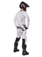 Alpinestars 2025 Racer Hollow Gear Set, blanco, vista trasera de un piloto de motocross con jersey y pantalones blancos con logotipos negros, casco negro y botas negras, conjunto profesional coordinado para carreras todoterreno