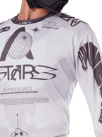 Primer plano del jersey Alpinestars Racer Hollow 2025, blanco y gris, con estampados gráficos negros con el logotipo del globo y código binario, ropa técnica de motocross para conducción off-road
