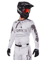 Alpinestars 2025 Racer Hollow Gear Set, conjunto de camiseta y pantalones de motocross, blanco con gráficos en negro y gris, con logotipos 'ASTARS' y diseños de globos huecos, combinado con casco negro, gafas de espejo rojas y guantes negros, diseñado para el rendimiento todoterreno