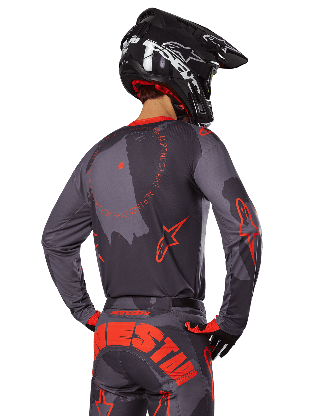 Alpinestars 2025 Racer Hollow Jersey, vista trasera de un piloto de motocross con equipamiento en Gris Camo y Naranja Flúor, con pantalones de camuflaje a juego con letras grandes de Alpinestars en naranja y un casco negro, diseño de ropa profesional para off-road.