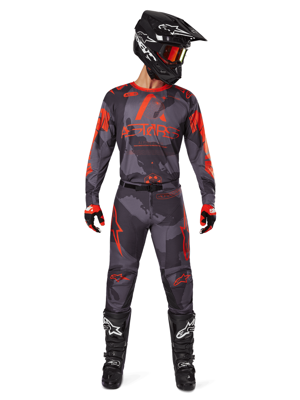 Piloto de motocross con jersey Alpinestars 2025 Racer Hollow y pantalones a juego en Gris Camo Naranja Fluo, conjunto de equipamiento completo con casco negro, gafas, guantes y botas, con logotipos naranjas llamativos y estampado de camuflaje.