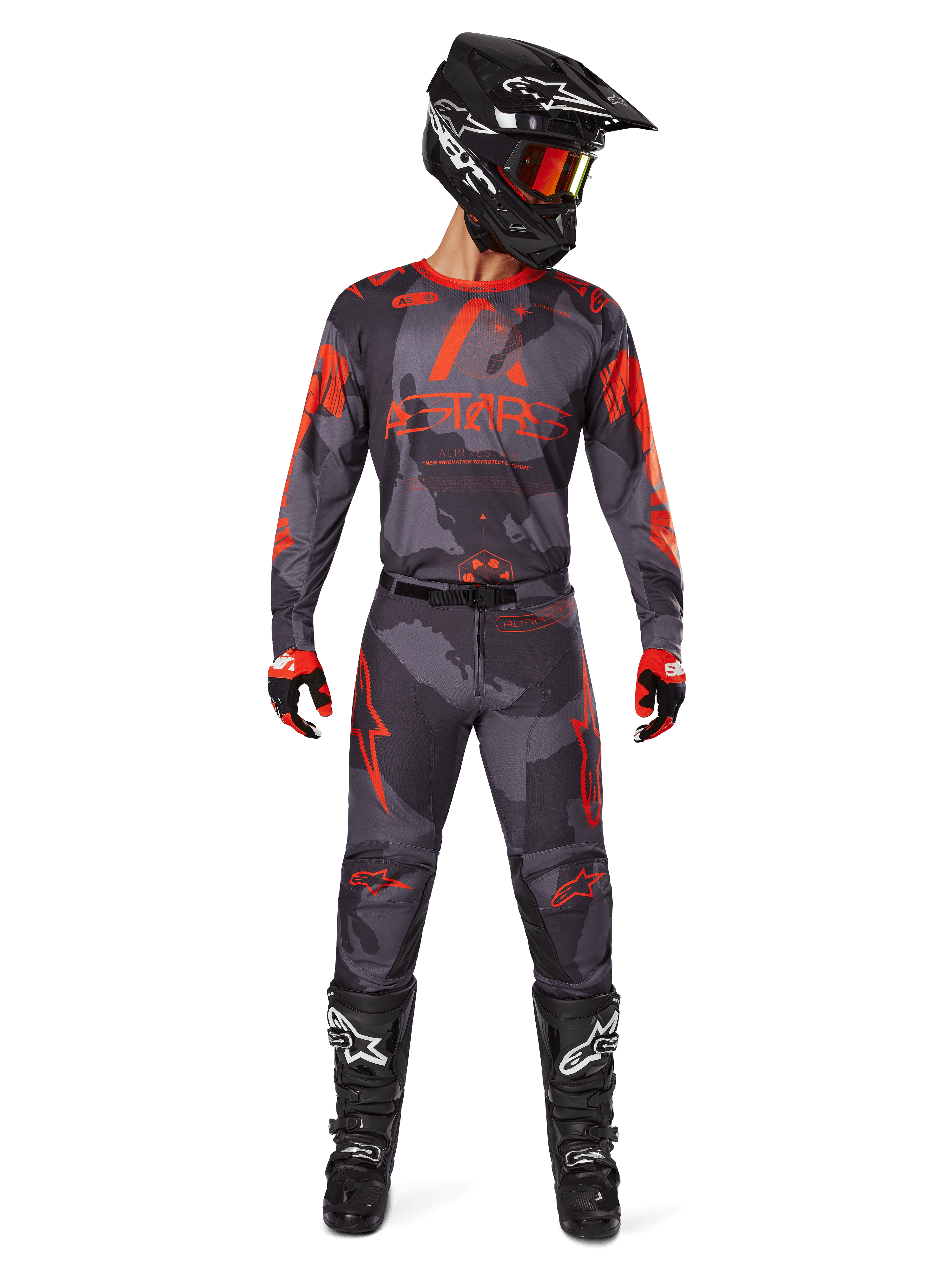 Piloto de motocross con jersey Alpinestars 2025 Racer Hollow y pantalones a juego en Gris Camo Naranja Fluo, conjunto de equipamiento completo con casco negro, gafas, guantes y botas, con logotipos naranjas llamativos y estampado de camuflaje.