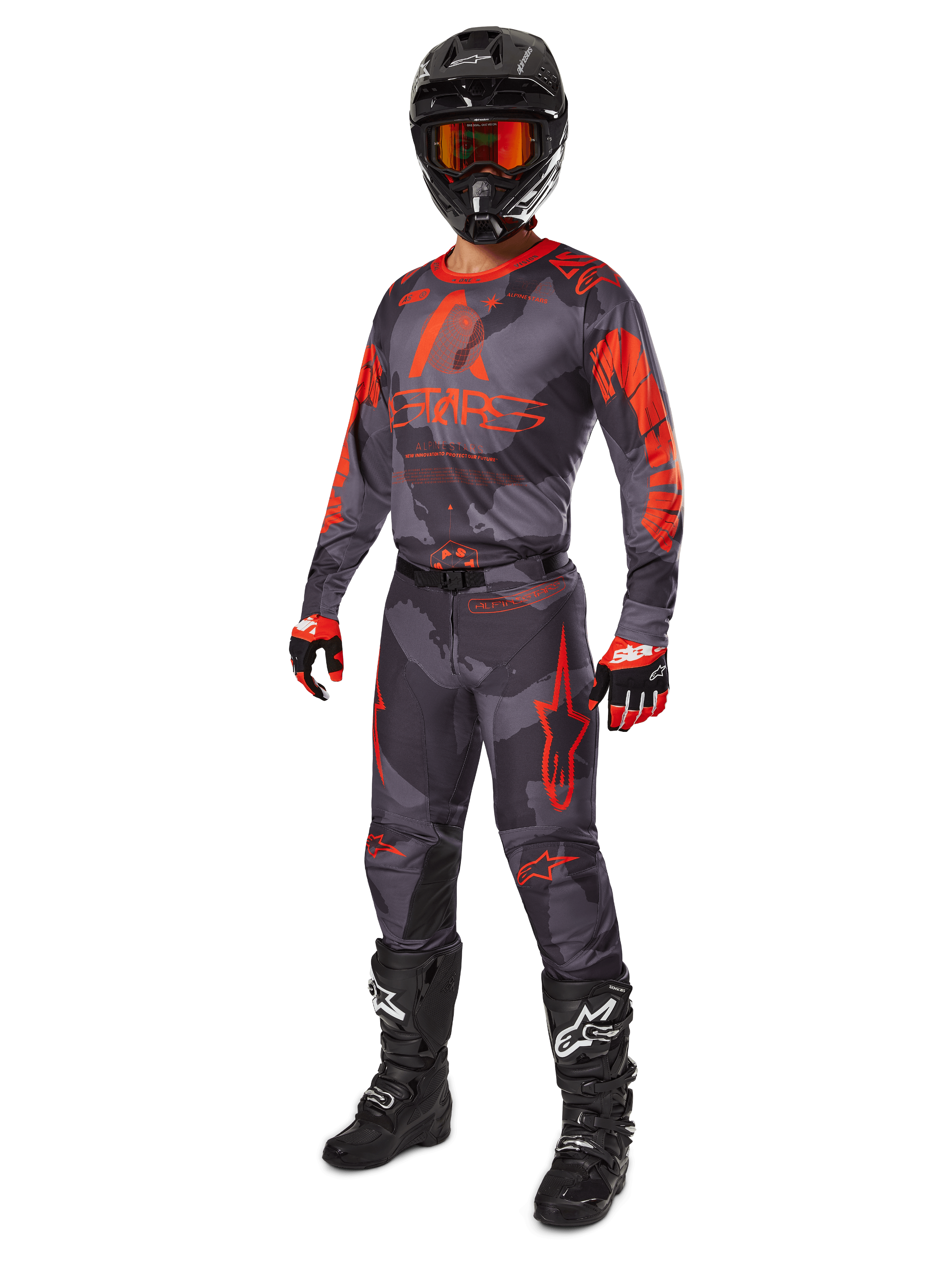 Piloto de motocross con equipamiento completo de competición, jersey y pantalones Alpinestars 2025 Racer Hollow en Gris Camo Naranja Flúor, casco negro con gafas naranjas, guantes negros y rojos, y botas negras con logotipos blancos, conjunto de alto rendimiento coordinado para carreras off-road