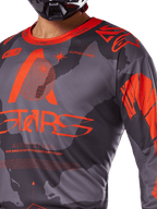 Alpinestars 2025 Racer Hollow Jersey, jersey de motocross, gris camuflaje y naranja flúor, con un gran logotipo naranja de Alpinestars y gráficos técnicos, cuello redondo, diseñado para un alto rendimiento en conducción off-road
