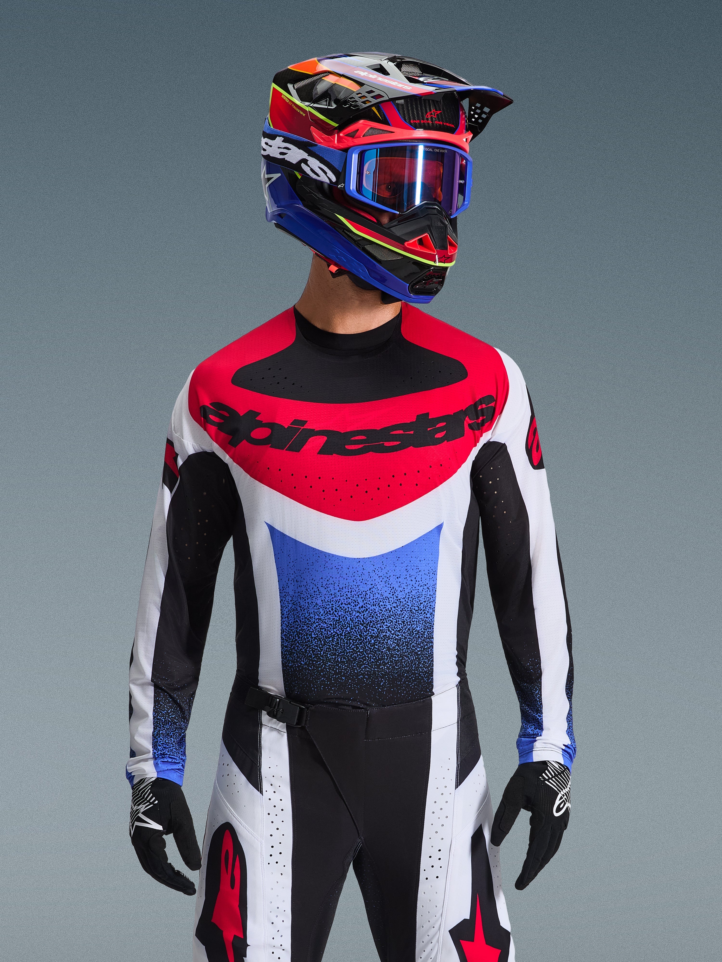 Alpinestars 2026 Techstar Knif Gear Set, piloto de motocross con equipamiento de competición completo, jersey rojo, blanco y azul con marca negra grande, pantalones negros y blancos a juego con el logo de la estrella roja, casco multicolor con gafas azules y guantes negros, conjunto coordinado para competición todoterreno