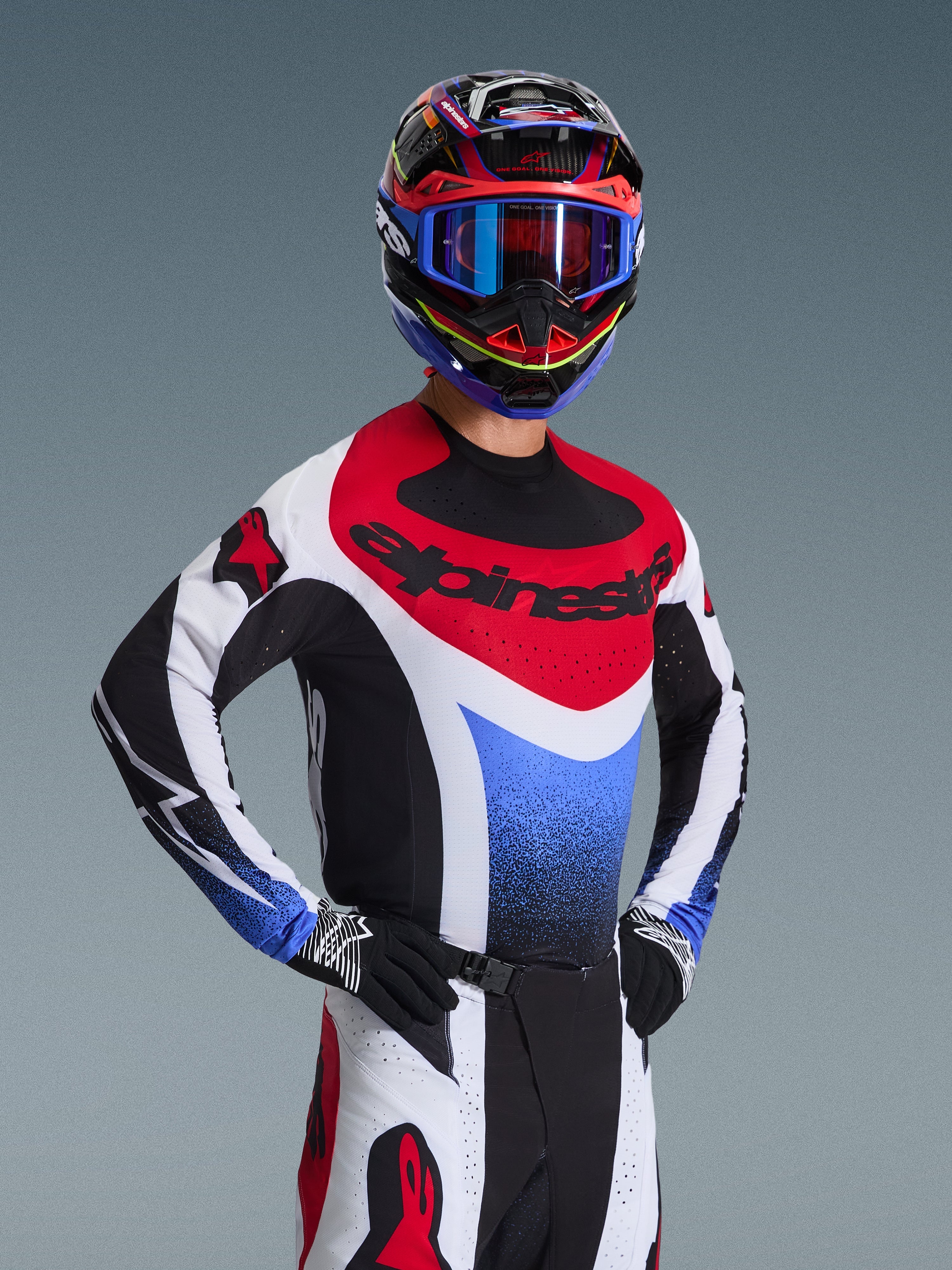 Alpinestars 2026 Techstar Knif Gear Set, piloto de motocross con jersey de carreras rojo, blanco y azul con detalles negros, casco y gafas multicolores a juego, guantes negros, equipo profesional para competición de motocross.