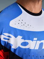 Alpinestars Techstar Knif Jersey 2026, jersey de motocross, primer plano del pecho y el cuello, azul y blanco con cuello negro, perforaciones de ventilación cortadas con láser, tejido de malla transpirable con el logo de Alpinestars.