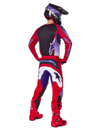 Piloto de motocross visto desde atrás con el conjunto Alpinestars 2025 Fluid Wurx, jersey morado y rojo brillante con panel trasero negro, pantalones de motocross a juego con detalles en blanco y morado, botas rojo brillante y casco negro, equipamiento profesional de carreras todoterreno