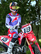 Piloto de motocross en una moto Honda CRF roja, vistiendo el jersey Alpinestars 2025 Fluid Wurx en púrpura y rojo brillante, pantalones a juego en púrpura y rojo, casco Red Bull con gafas amarillas, botas y guantes Alpinestars blancos, equipamiento profesional de MX para conducción todoterreno