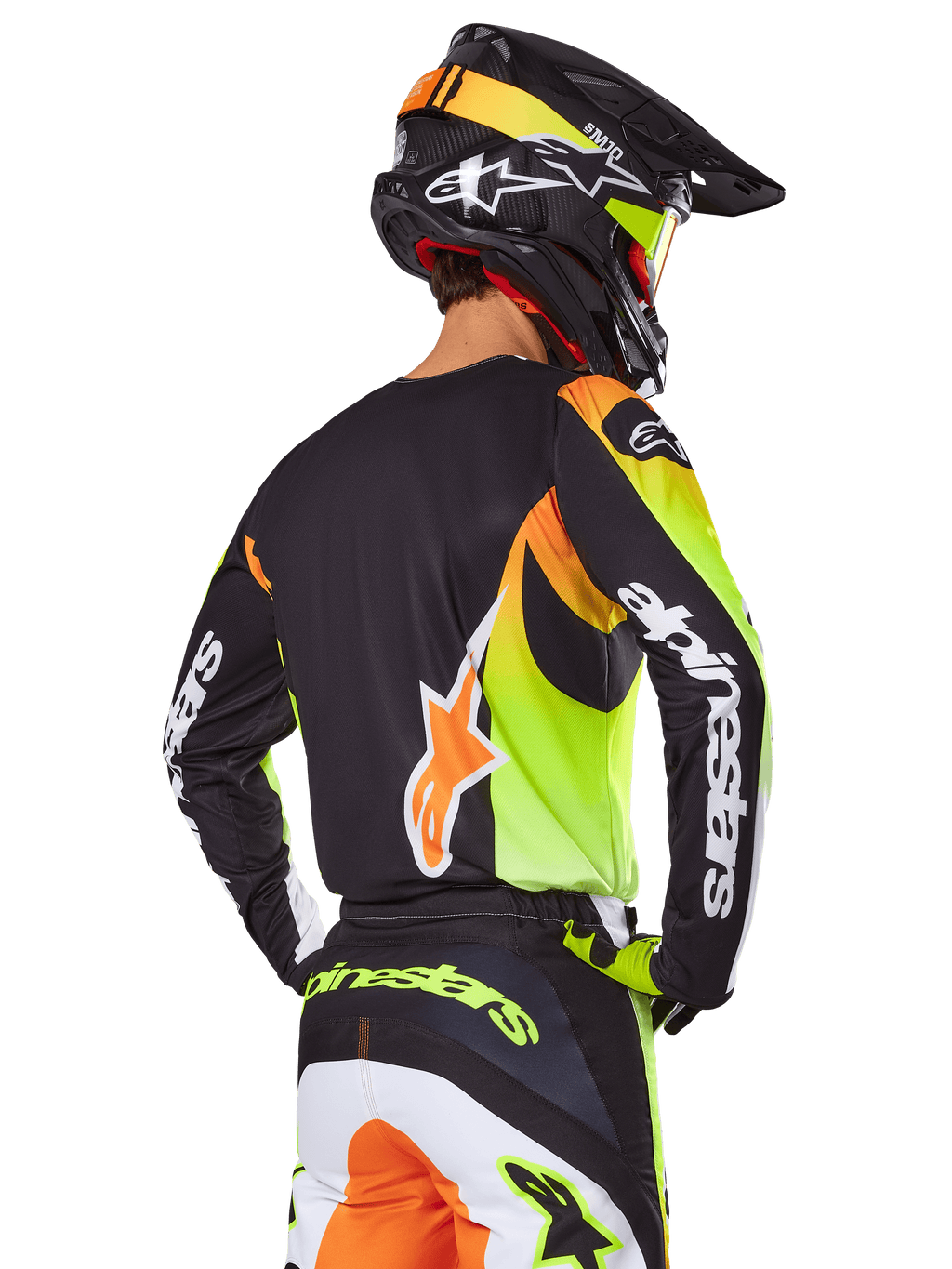 Piloto de motocross visto desde atrás con el conjunto de equipo Alpinestars 2025 Fluid Wurx, jersey negro con gráficos vibrantes en amarillo neón y naranja, pantalones a juego con paneles blancos y naranjas, casco negro con detalles neón, logotipo destacado de Alpinestars en las mangas y el asiento