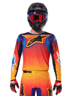 Jersey Alpinestars Fluid Wurx 2025, jersey de motocross multicolor con degradado naranja y rojo y detalles en púrpura, usado con equipamiento a juego, casco negro con gafas azules y rojas, y guantes rojos, con un gran logotipo de estrella negra en el pecho.