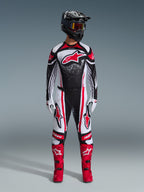 Piloto de motocross con equipamiento completo de Alpinestars, Jersey Techstar Nomur 2026 en negro, blanco y rojo, pantalones a juego con detalles rojos, casco negro y botas rojas brillantes, con un gran logotipo Astars rojo en el pecho y patrón de degradado moteado, conjunto coordinado para competición todoterreno