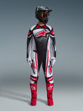 Piloto de motocross con el conjunto de equipo Alpinestars 2026 Techstar Nomur, negro, blanco y rojo, jersey con un gran logo de estrella roja y patrón moteado, pantalones a juego con paneles laterales rojos, casco negro con gafas ahumadas y botas de motocross rojas