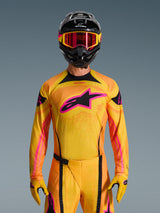 Alpinestars Techstar Nomur Jersey 2026 en naranja, amarillo y rosa, lucido por un piloto de motocross con casco negro y gafas rosas a juego, con un gran logotipo rosa de Alpinestars en el pecho, ajuste atlético de competición para rendimiento off-road.