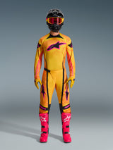 Piloto de motocross con el Jersey Techstar Nomur 2026 en naranja, amarillo y rosa, combinado con pantalones de motocross a juego, casco negro con gafas rosas y botas rosa vibrante, equipamiento de ajuste de carrera atlético para competición todoterreno
