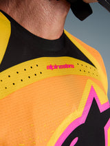 Alpinestars Techstar Nomur Jersey 2026, jersey de motocross, naranja, amarillo y rosa, detalle de primer plano del pecho y el cuello con ventilación cortada con láser, logotipo en color rosa y tejido de malla transpirable