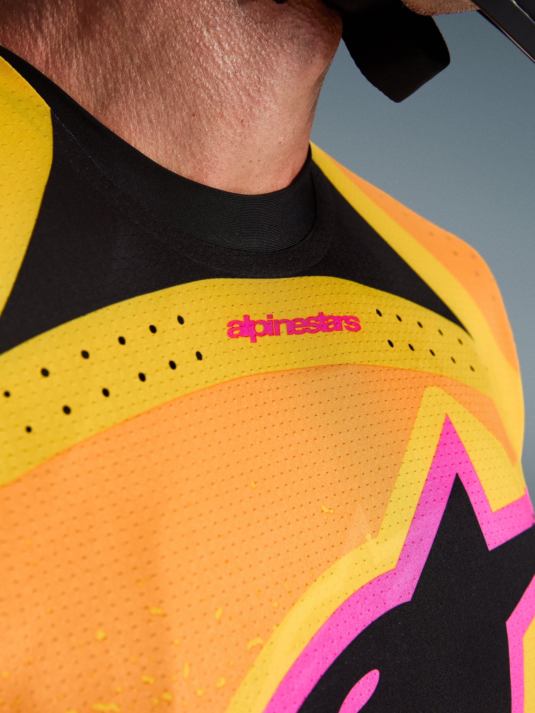 Alpinestars Techstar Nomur Jersey 2026, jersey de motocross, naranja, amarillo y rosa, detalle de primer plano del pecho y el cuello con ventilación cortada con láser, logotipo en color rosa y tejido de malla transpirable