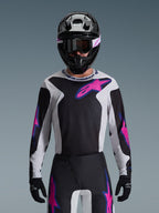Alpinestars 2026 Fluid Grid Jersey, jersey de motocross, negro, gris claro y púrpura, usado por un piloto con pantalones off-road a juego, casco negro y gafas, conjunto completo de equipamiento de alto rendimiento para competición