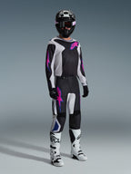 Piloto de motocross con equipamiento completo de carreras, Jersey Fluid Grid 2026 en negro con detalles en gris claro y púrpura, pantalones Fluid Grid a juego, casco negro con gafas coordinadas, botas blancas y negras, y guantes negros, en un estudio profesional para carreras off-road.