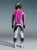 Alpinestars 2026 Fluid Grid Jersey y pantalones a juego, conjunto de equipamiento de motocross, rosa, blanco y púrpura, vista trasera que muestra el ajuste atlético ergonómico, usado con un casco negro y botas blancas, diseñado para el rendimiento off-road.