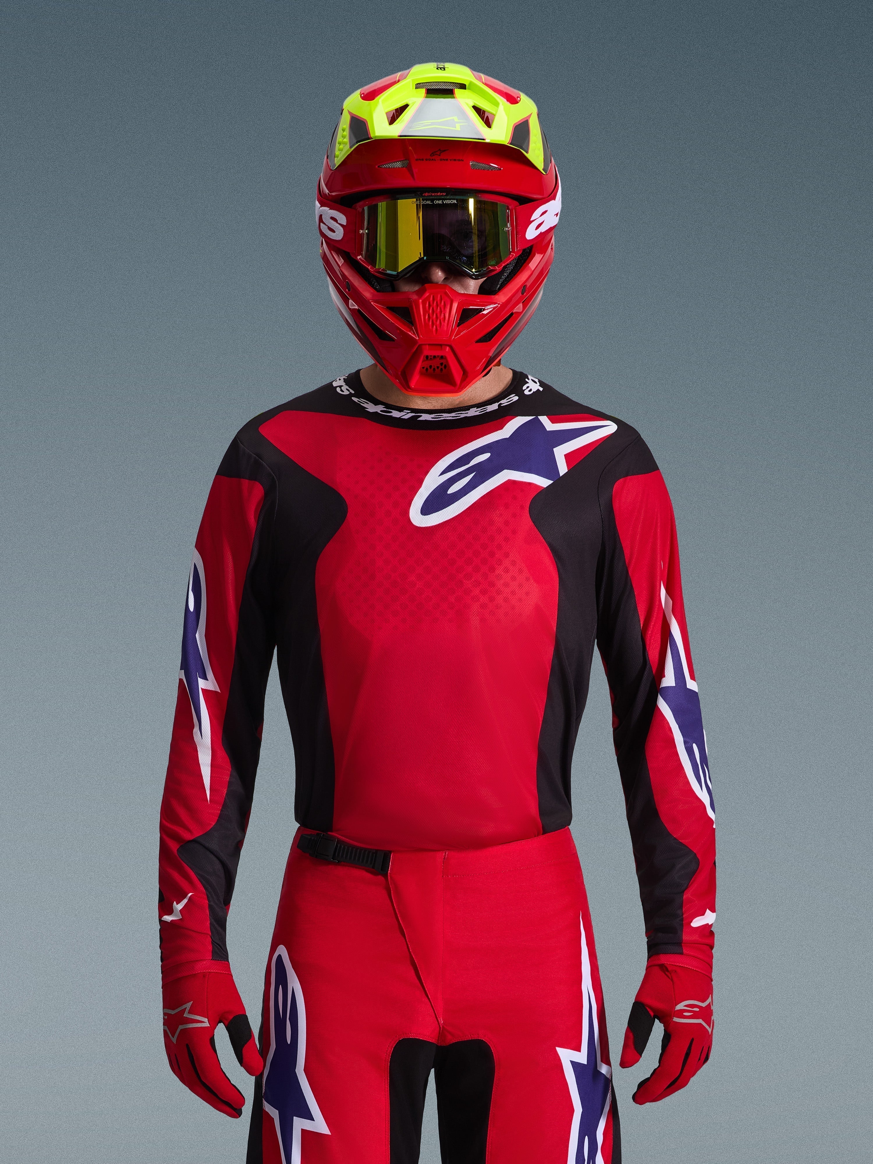 Alpinestars 2026 Fluid Grid Jersey, jersey de motocross, rojo, negro y púrpura, usado por un piloto con casco rojo y amarillo neón y gafas doradas, con grandes logotipos de estrella en el pecho y las mangas, equipamiento coordinado para carreras todoterreno