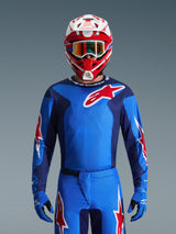 Alpinestars 2026 Fluid Grid Jersey, jersey de motocross azul y rojo, combinado con pantalones a juego y un casco rojo y blanco, con destacados logotipos de estrellas rojas y un ajuste atlético diseñado para el rendimiento en carreras todoterreno