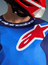 Alpinestars 2026 Fluid Grid Jersey, azul y rojo, vista de cerca del pecho y el cuello deportivo, logotipo grande de la estrella de Alpinestars en rojo y blanco, marca Alpinestars en el cuello, usado con un casco rojo y blanco