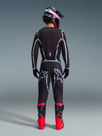 Piloto de motocross desde atrás con el Jersey Alpinestars 2026 Fluid Apex y pantalones a juego en negro/gris, con líneas de diseño geométricas blancas y logotipos de estrella en el asiento, complementado con un casco negro y rosa y botas de competición rojas y negras