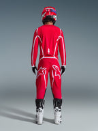 Rear view of a motocross rider wearing the Alpinestars 2026 Fluid Apex Gear Set, bright red jersey and pants with white stripes and logos, paired with white and black boots and a red helmet, professional off-road racing kit
