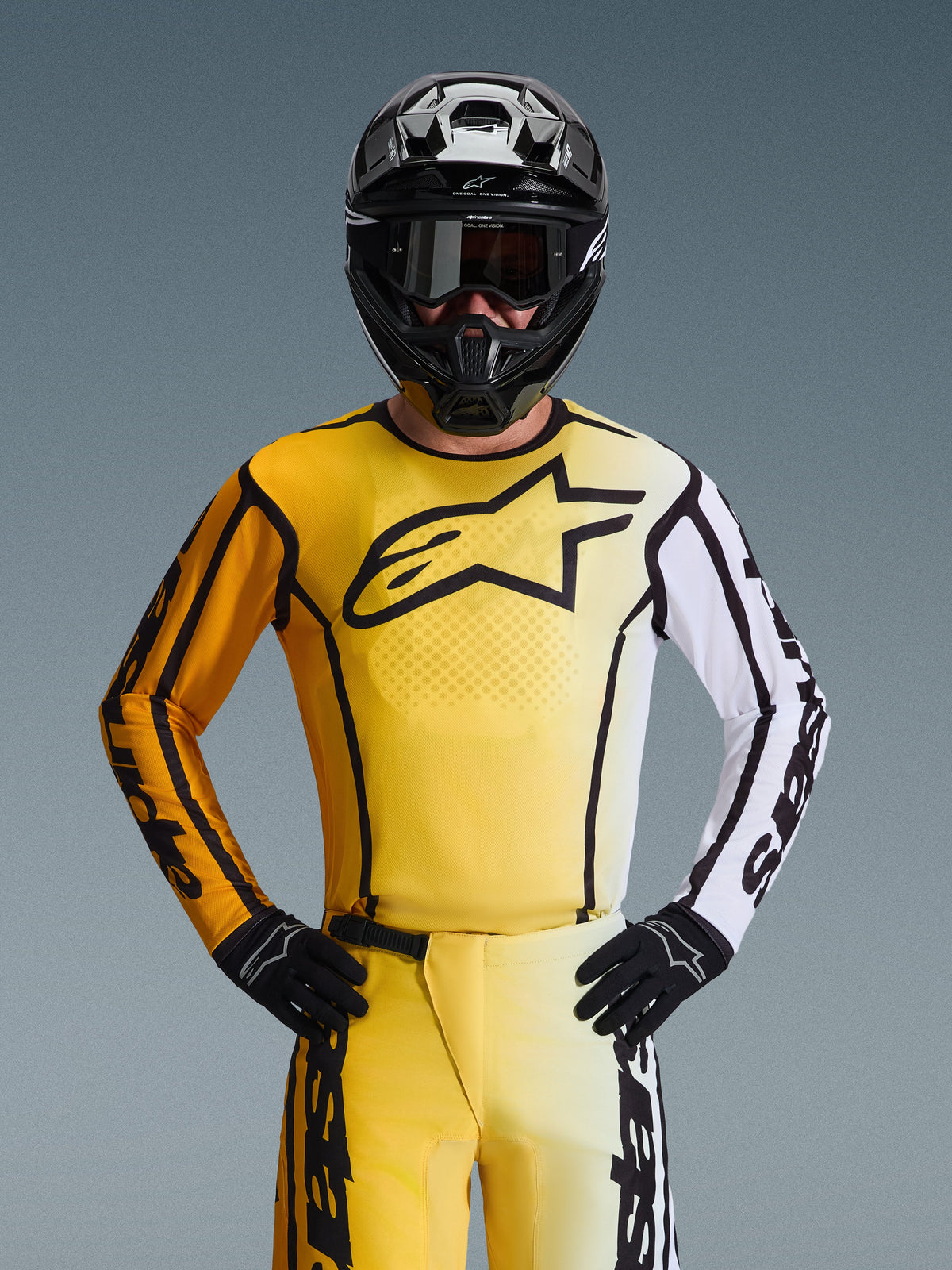 Alpinestars 2026 Fluid Apex Jersey, jersey de motocross, amarillo y negro con una manga blanca y un gran logotipo negro en el pecho, usado como parte de un conjunto completo de equipamiento de carreras con pantalones a juego, casco negro y guantes