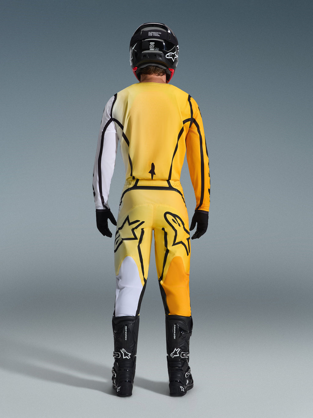 Motocross rider from behind wearing Alpinestars 2026 Fluid Apex Jersey and matching pants in Yellow Black, featuring bold color-blocked panels in white, yellow, and orange, paired with a black helmet and motocross boots.