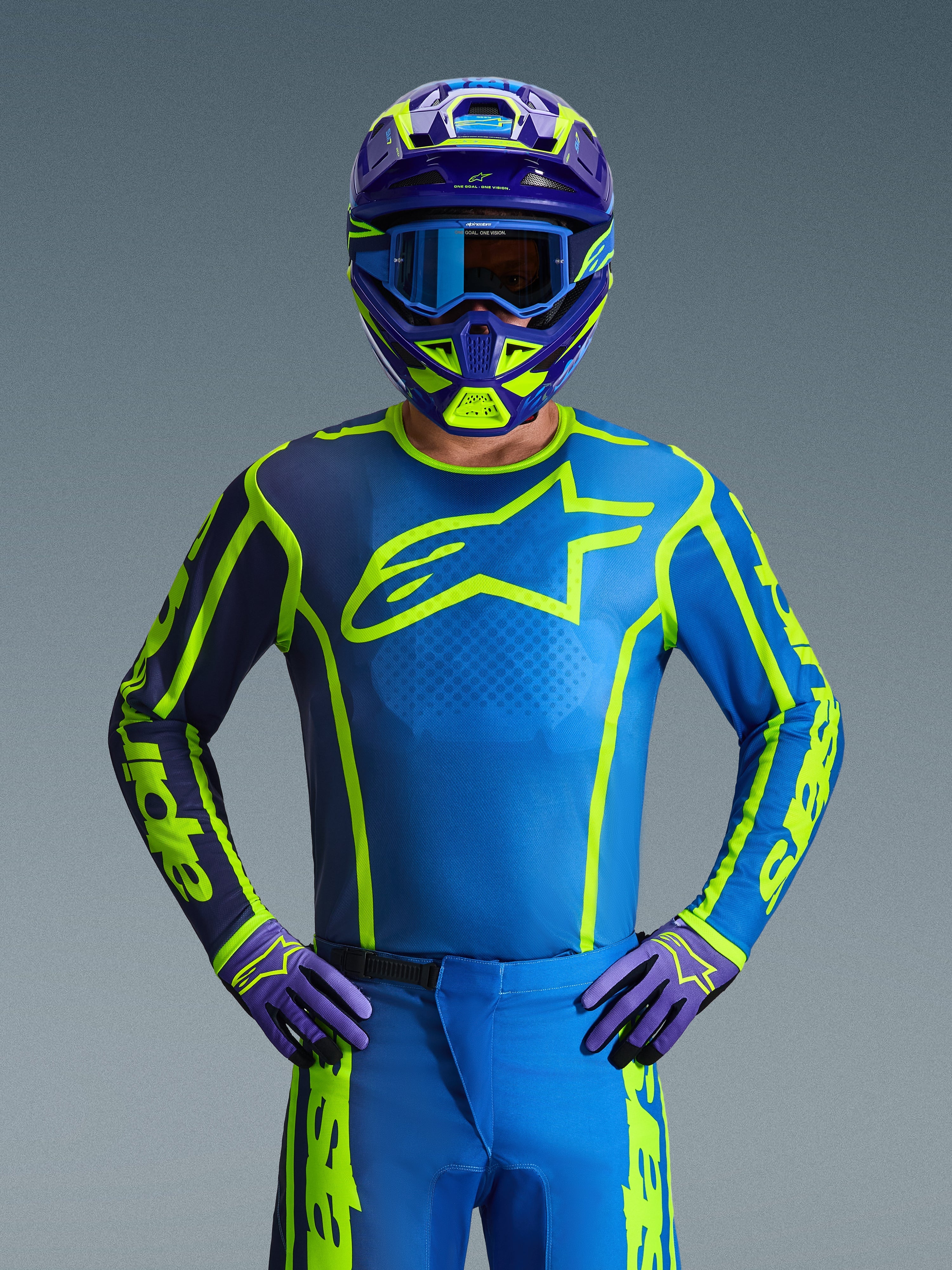 Piloto de motocross con el Jersey Alpinestars Fluid Apex 2026 en Azul Amarillo Flúor, con una base azul vibrante, gráficos en amarillo fluorescente y un gran logotipo en el pecho, coordinado con casco y guantes a juego, diseñado para carreras de motocross y todoterreno
