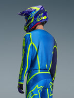 Alpinestars 2026 Fluid Apex Jersey, Azul Amarillo Flúor, vista trasera de un piloto con pantalones de motocross y casco a juego, con gráficos geométricos en amarillo fluorescente y un ajuste atlético relajado, equipamiento coordinado para carreras off-road