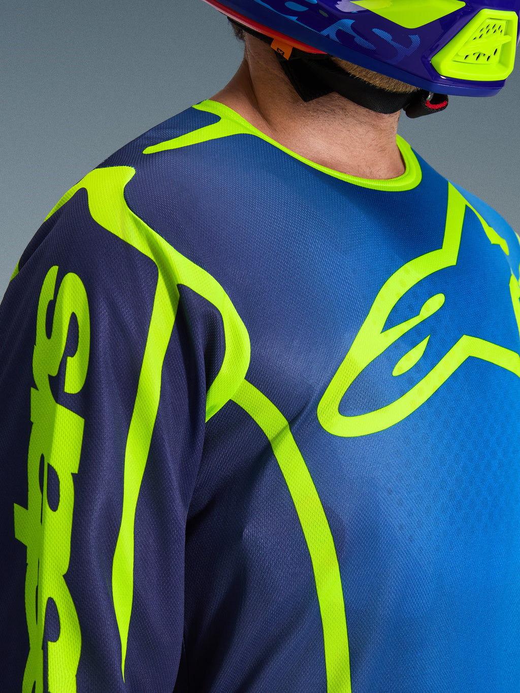 Alpinestars Jersey Fluid Apex 2026, jersey de motocross en azul y amarillo flúor, vista de primer plano que muestra el gran logotipo del pecho en amarillo neón y la marca en la manga, construcción en tejido polifabric transpirable con cuello deportivo ergonómico