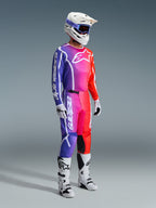 Piloto de motocross con equipamiento completo de competición, Jersey y Pantalones Fluid Apex 2026 con un degradado vibrante de púrpura, rosa y naranja, casco blanco con gafas azules, botas blancas y negras, y guantes blancos, conjunto coordinado para motocross todoterreno