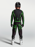 Pantalones Alpinestars Fluid Apex V2, equipo de motocross negro y verde flúor, vista posterior del piloto con botas blancas.