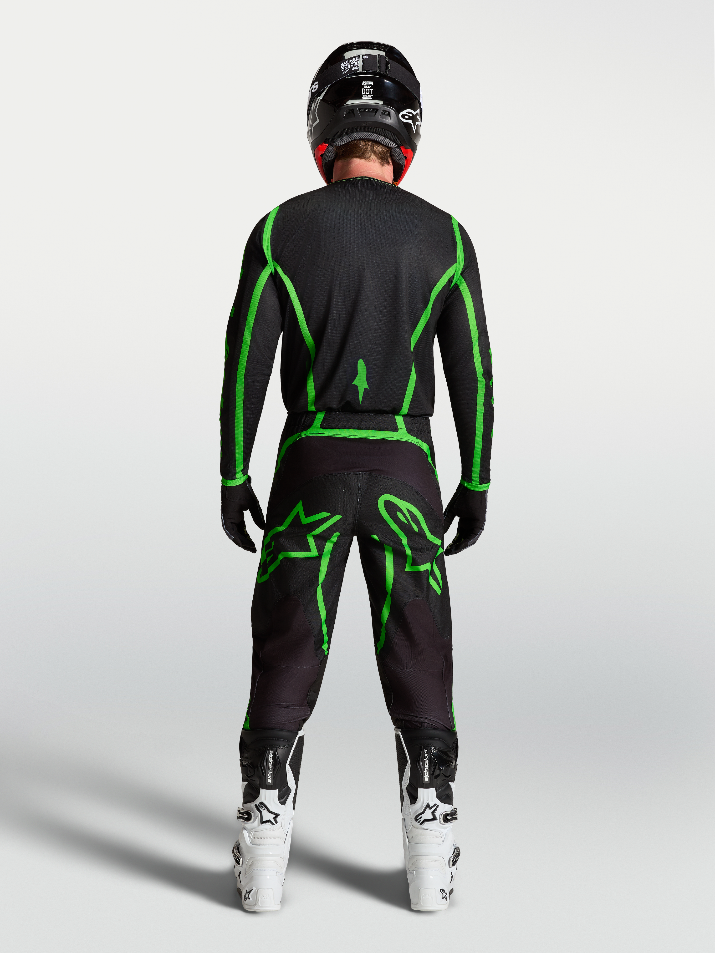 Pantalones Alpinestars Fluid Apex V2, equipo de motocross negro y verde flúor, vista posterior del piloto con botas blancas.